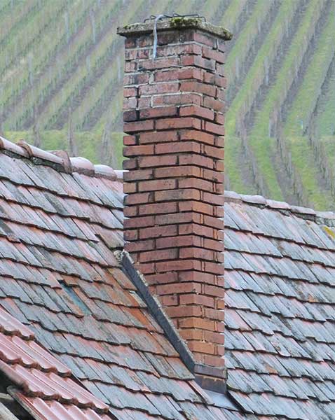 Stock photo of tall leaky chimney on slate roof - West Tennessee Chimneys Leaky chimney tall moss covered with spalding on slate roof